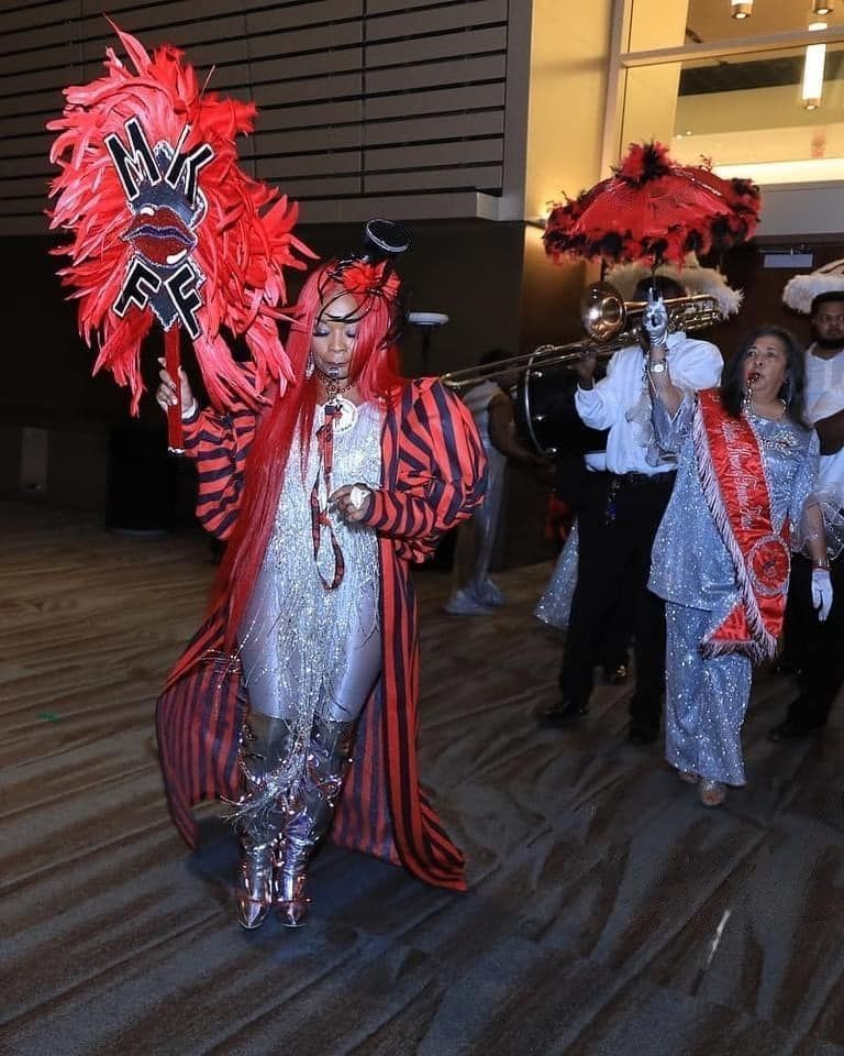A woman in a red and silver costume is holding a fan