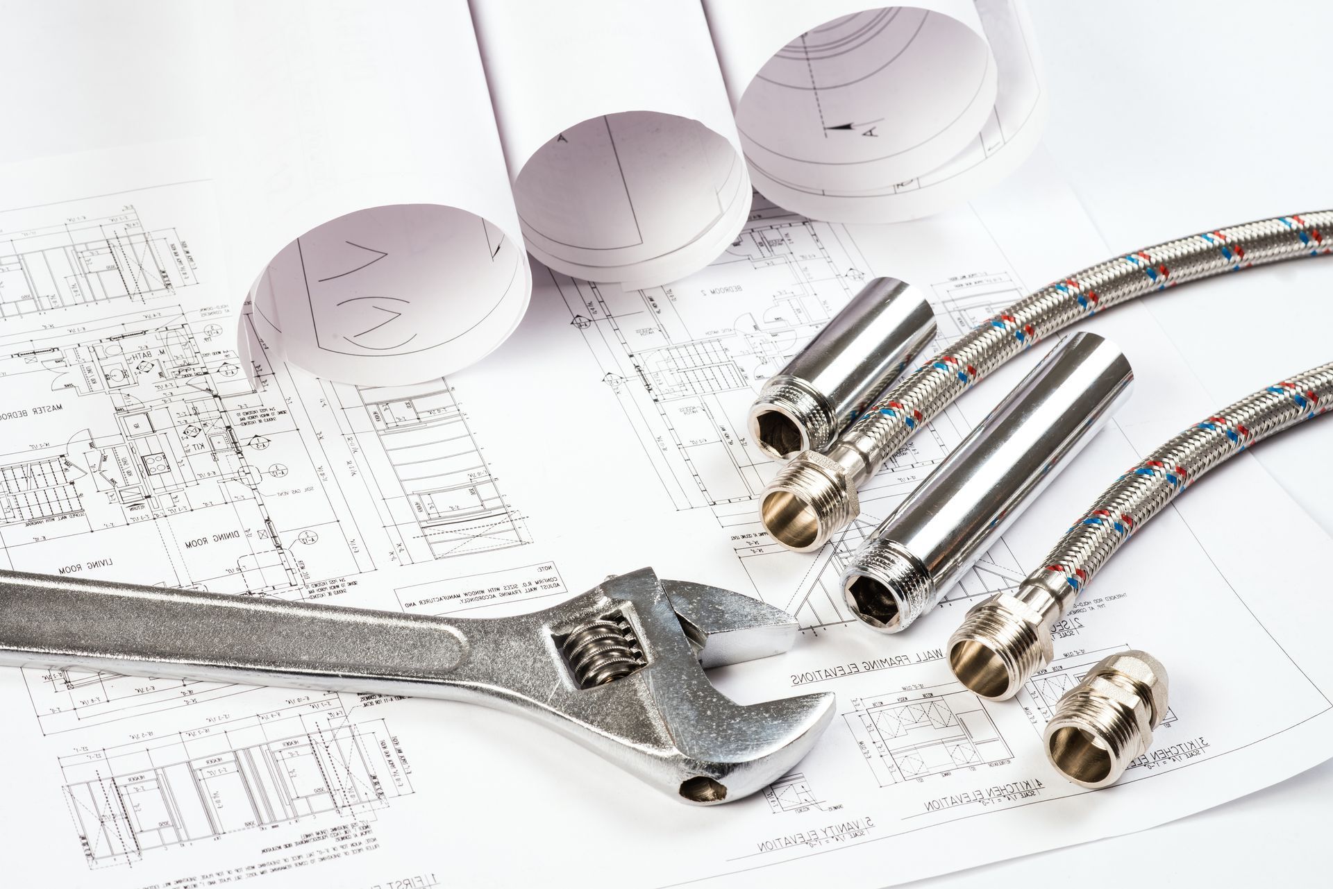 Clé, pièces de plomberie et plans sur une surface blanche, suggérant des travaux de construction ou de réparation.