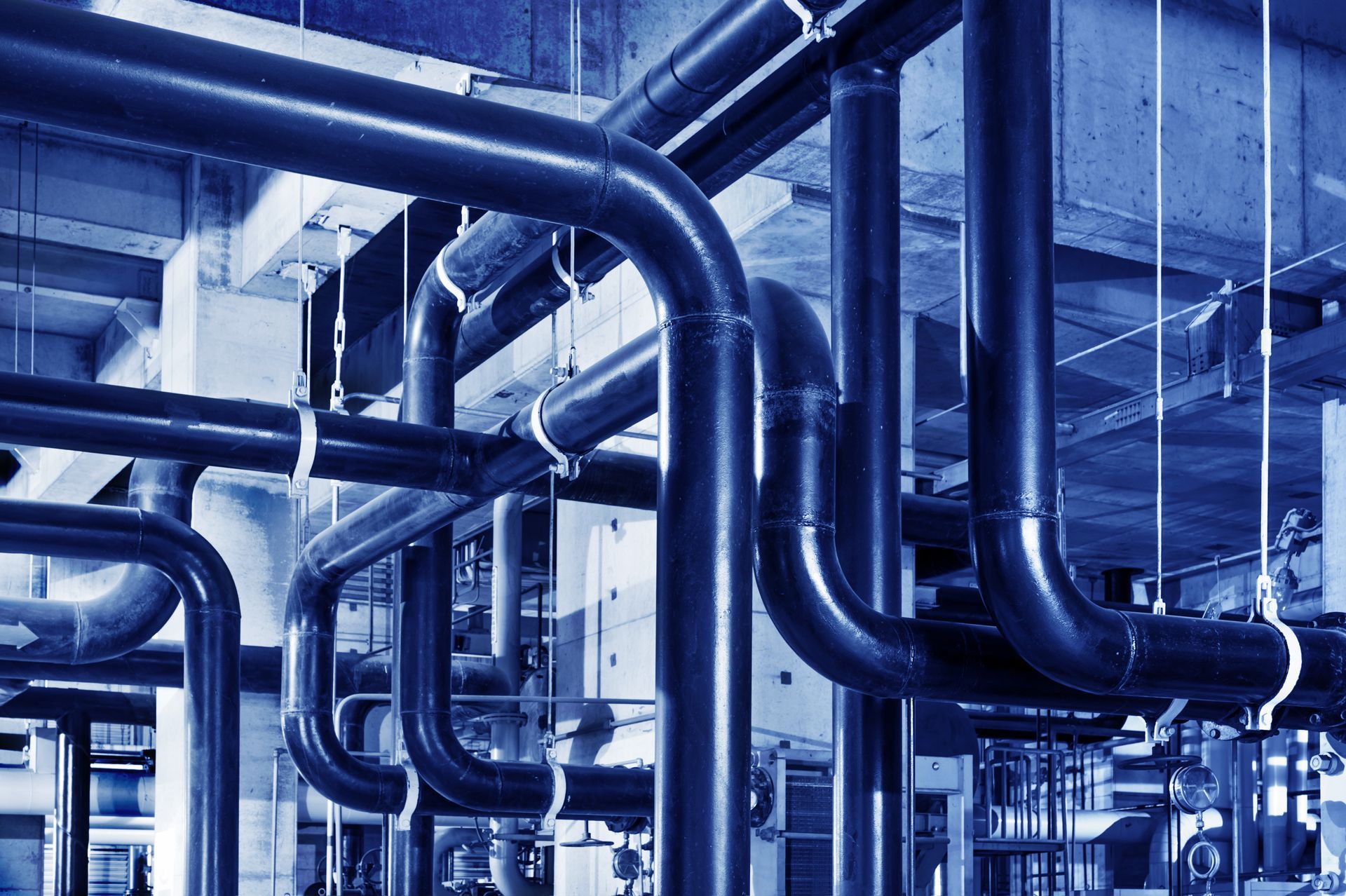 Photographie aux tons bleus d'un réseau de tuyaux industriels et de plomberie dans une usine.