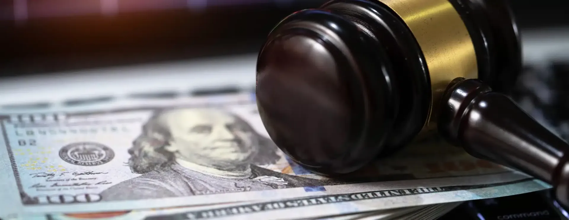 A gavel rests on top of a stack of US one-hundred dollar bills.