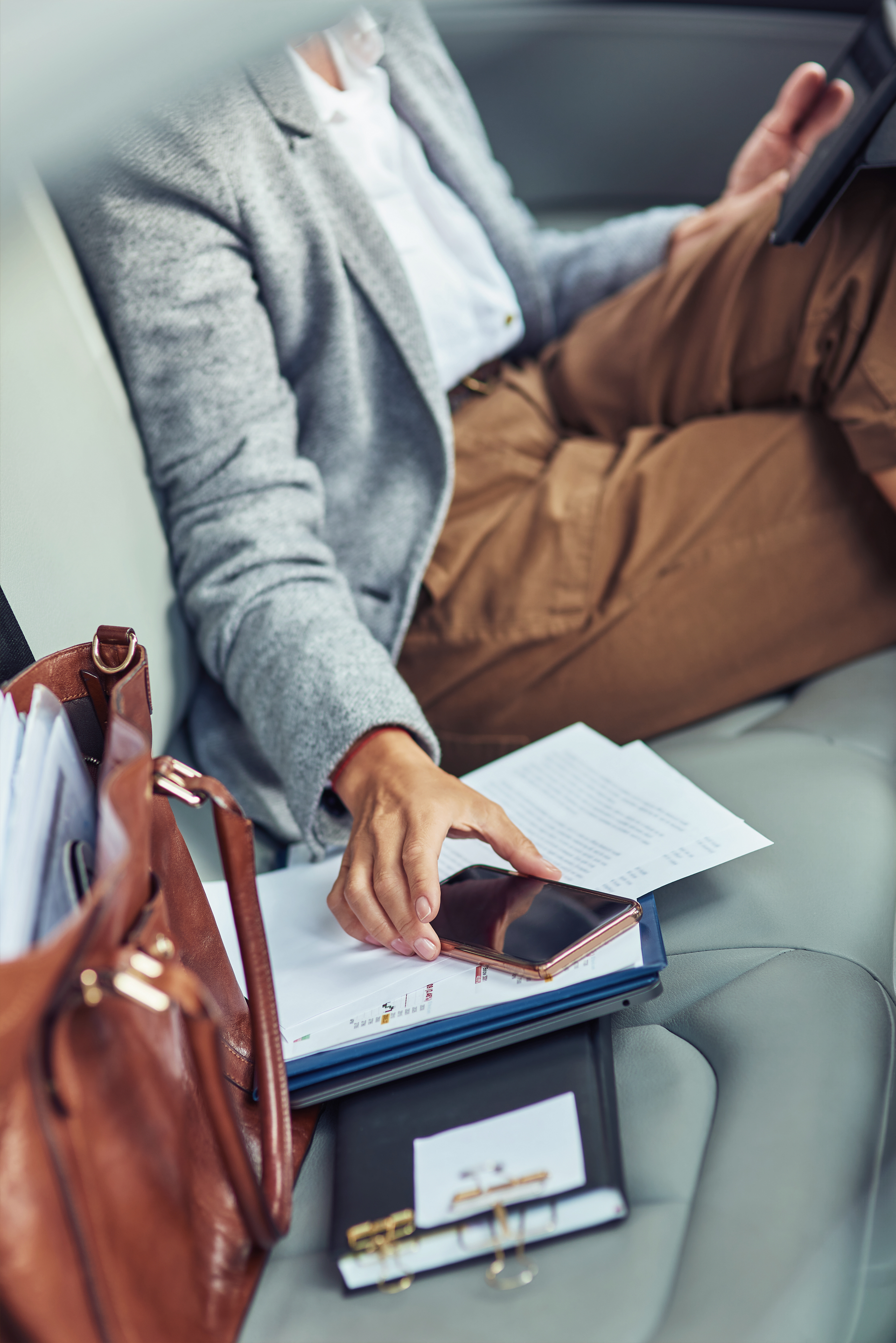 Person in a car holding a phone, sitting with a briefcase and documents.