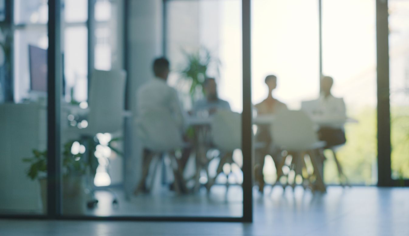 Blurred view of people in a meeting at a light-filled office.