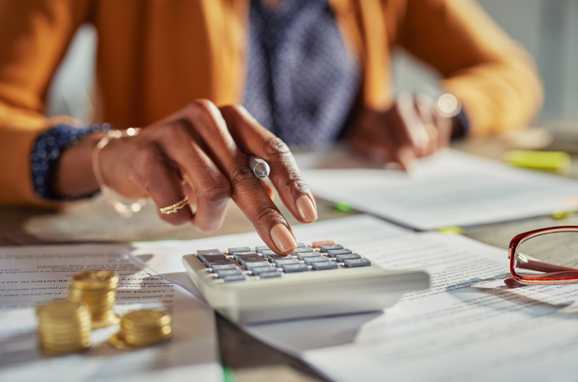 Woman's hand using a calculator, with coins and documents on a desk, possibly financial.