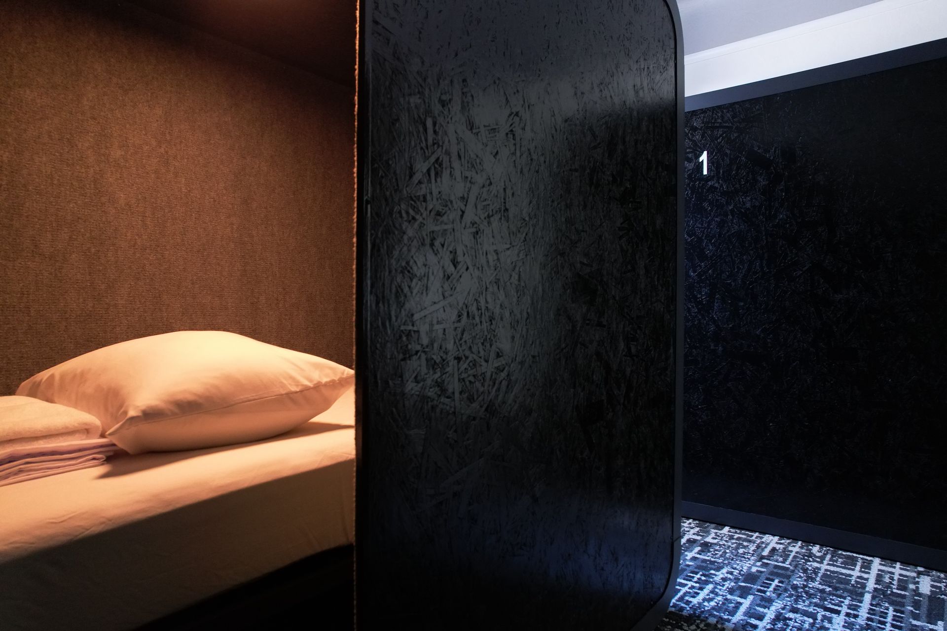 A small hotel room with a bed and a dark entryway labeled 