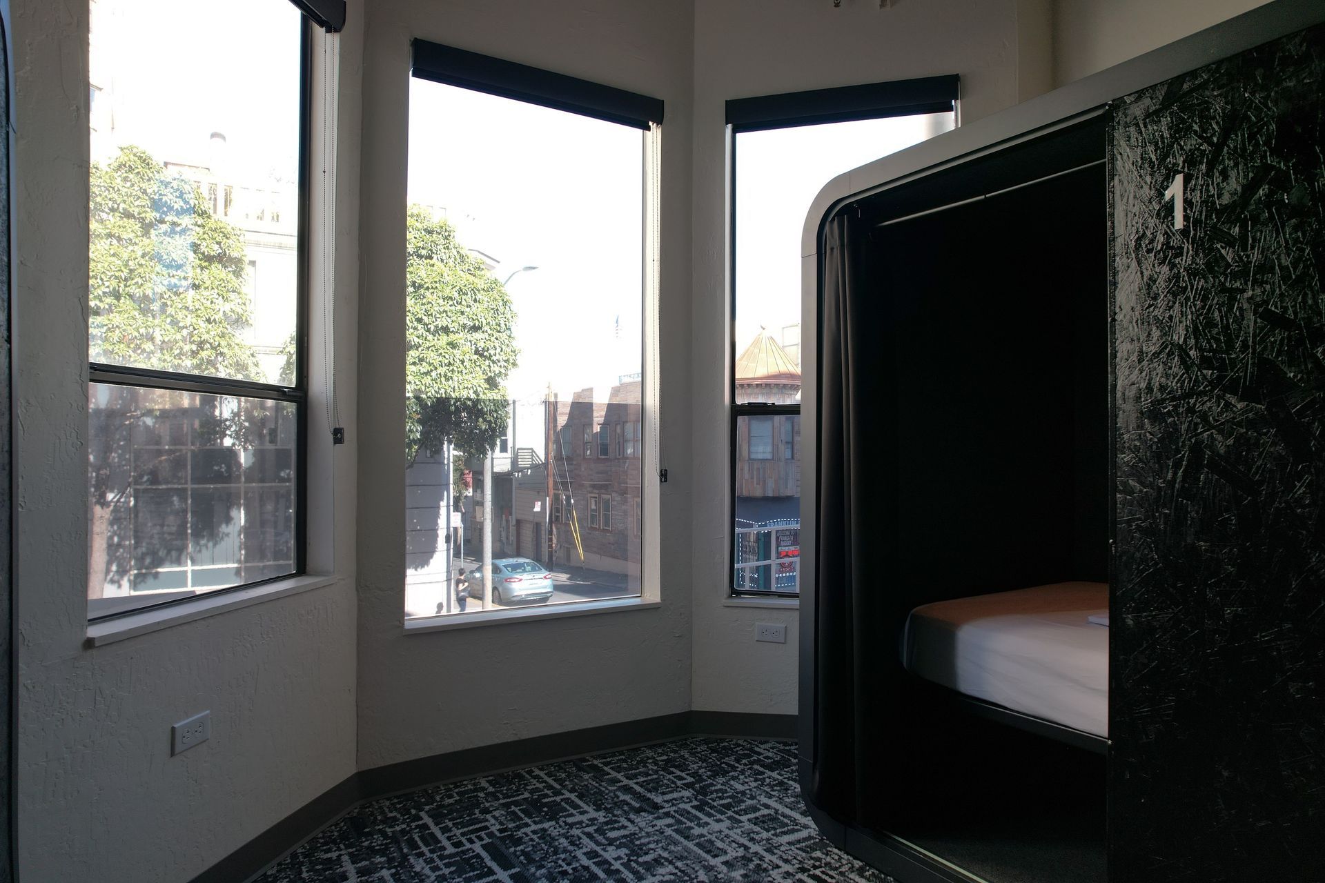 Small, dark hotel room with a bed and a bathroom behind glass.