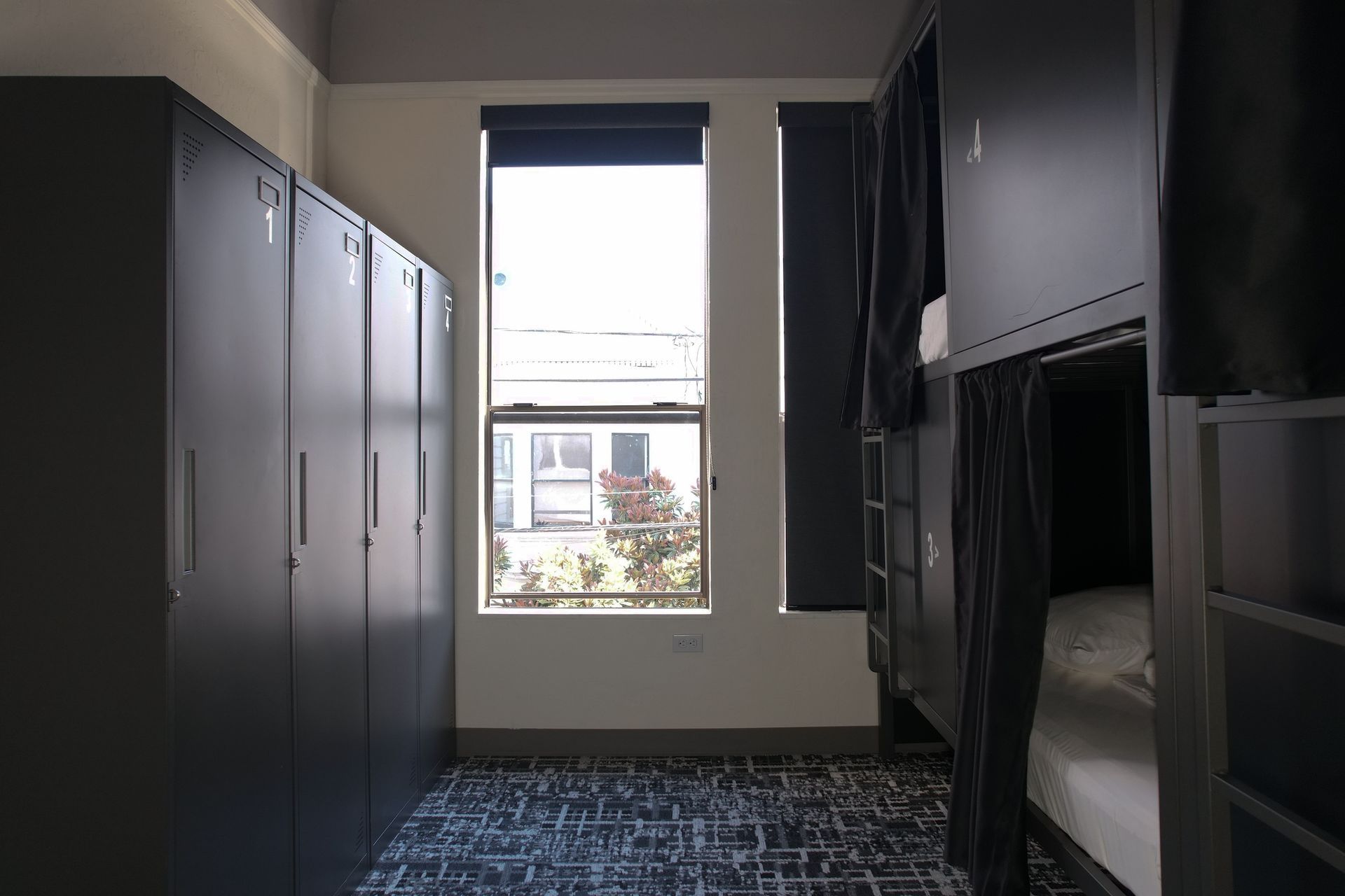 Hostel dorm room: bunk beds, lockers, window with view of building.