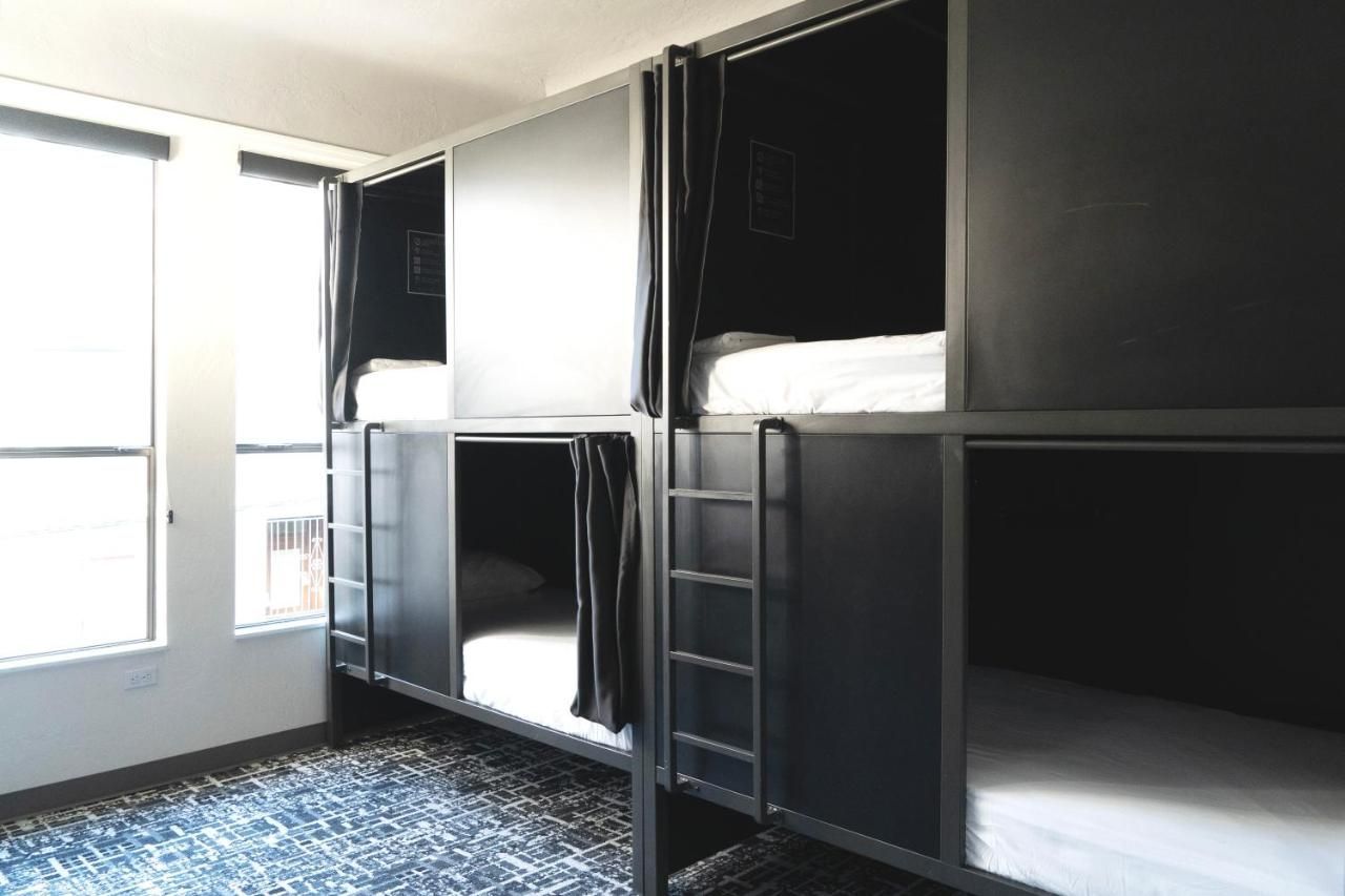 Bunk beds in a room with black frames, white mattresses, and curtains for privacy. A window is in the background.