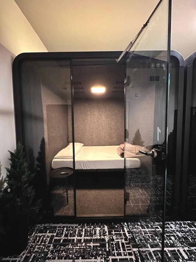 Small, dark hotel room with a bed and a bathroom behind glass.