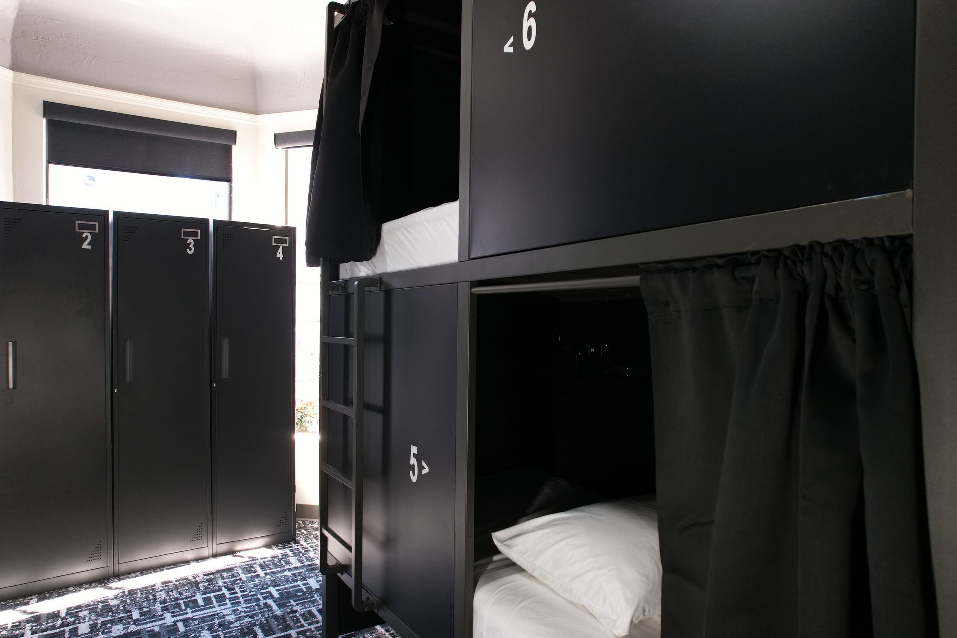 Dorm room interior with black bunk beds, lockers, and a patterned blue and white carpet.