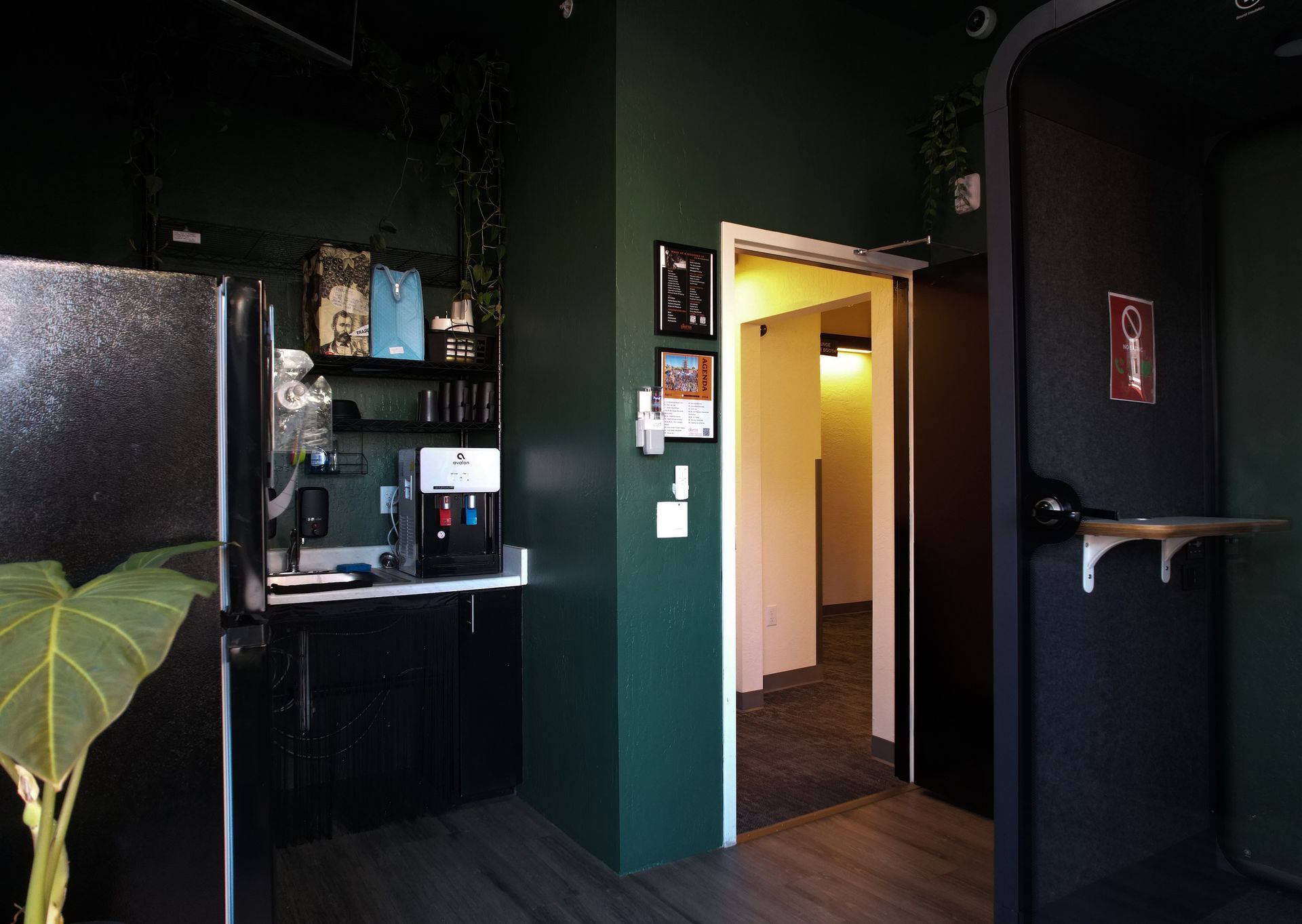 Office space with a dark green wall, refrigerator, and doorway to a hallway.