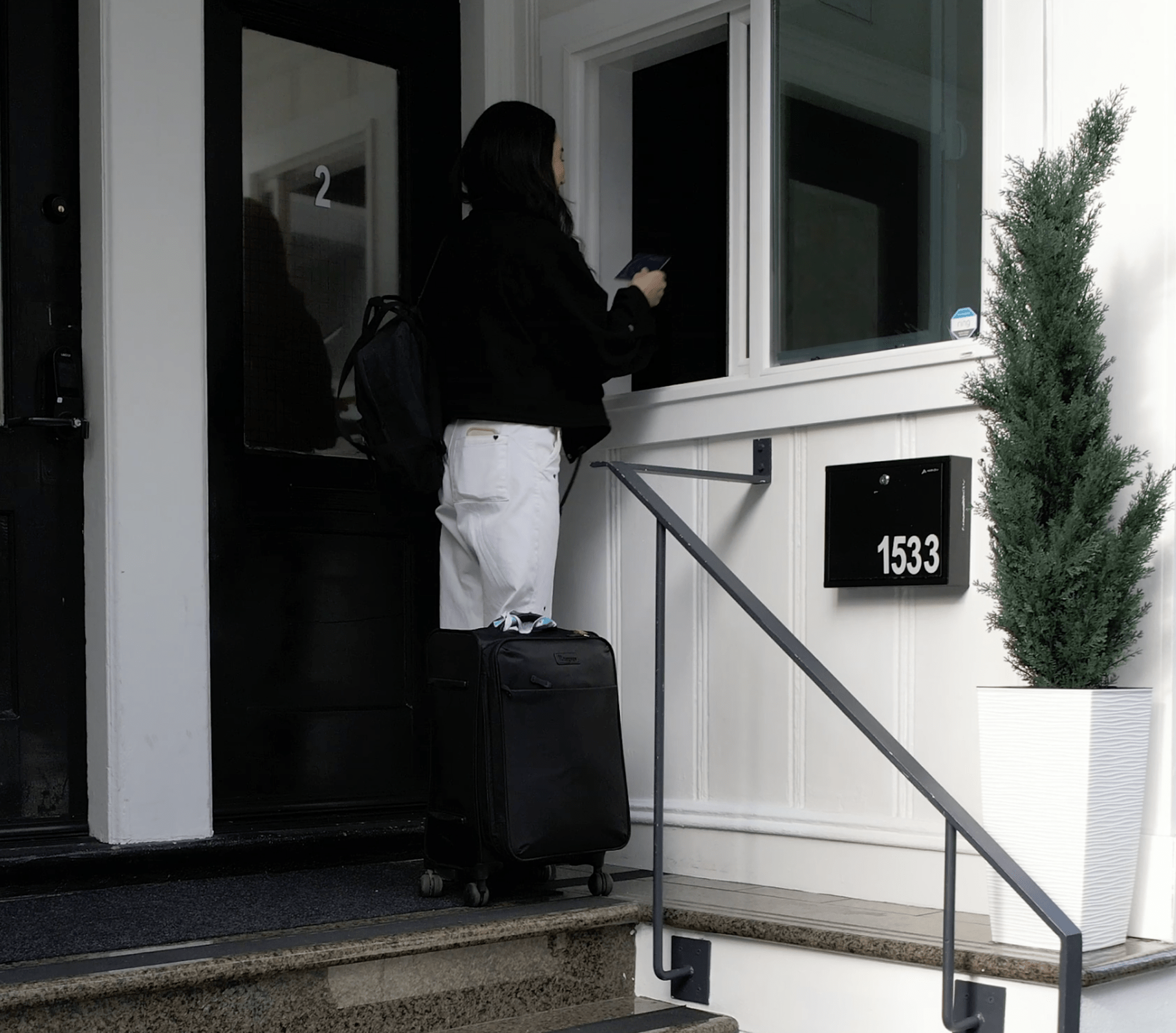 Person unlocking a door with a suitcase, standing on steps outside a house.