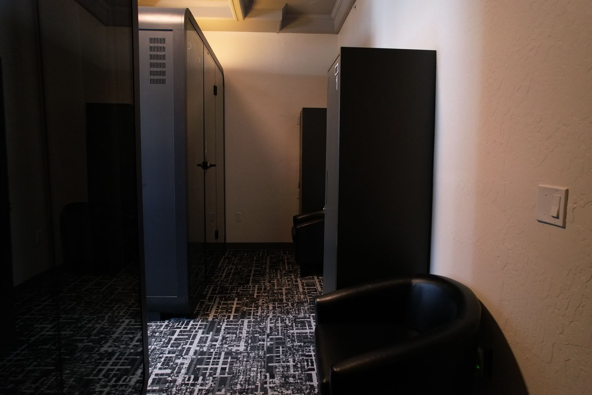 Dark, minimalist capsule hotel room with a bed and towels, viewed through glass. Number 1 on the wall.