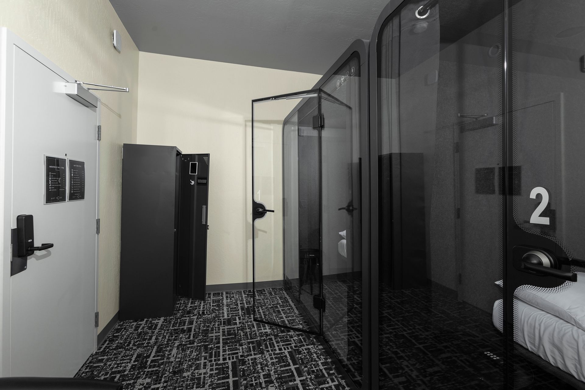 Hotel room hallway with glass pods, door, lockers, and patterned carpet.