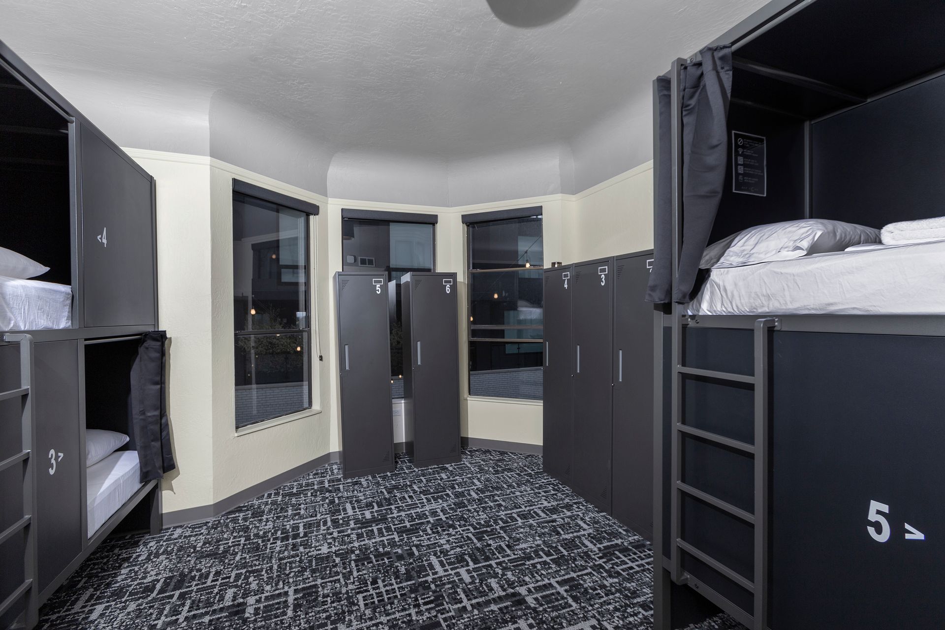 Black capsule hotel room with a bed inside, a door and a wardrobe.