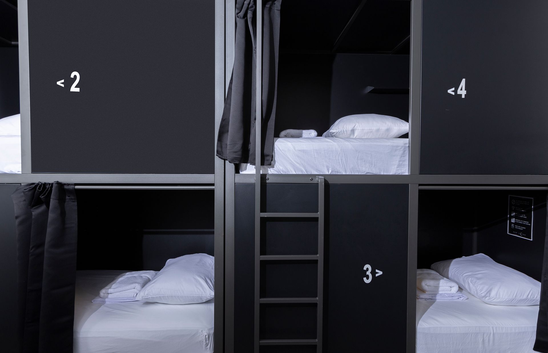 A small, minimalist hotel room with a bed and a black door marked 