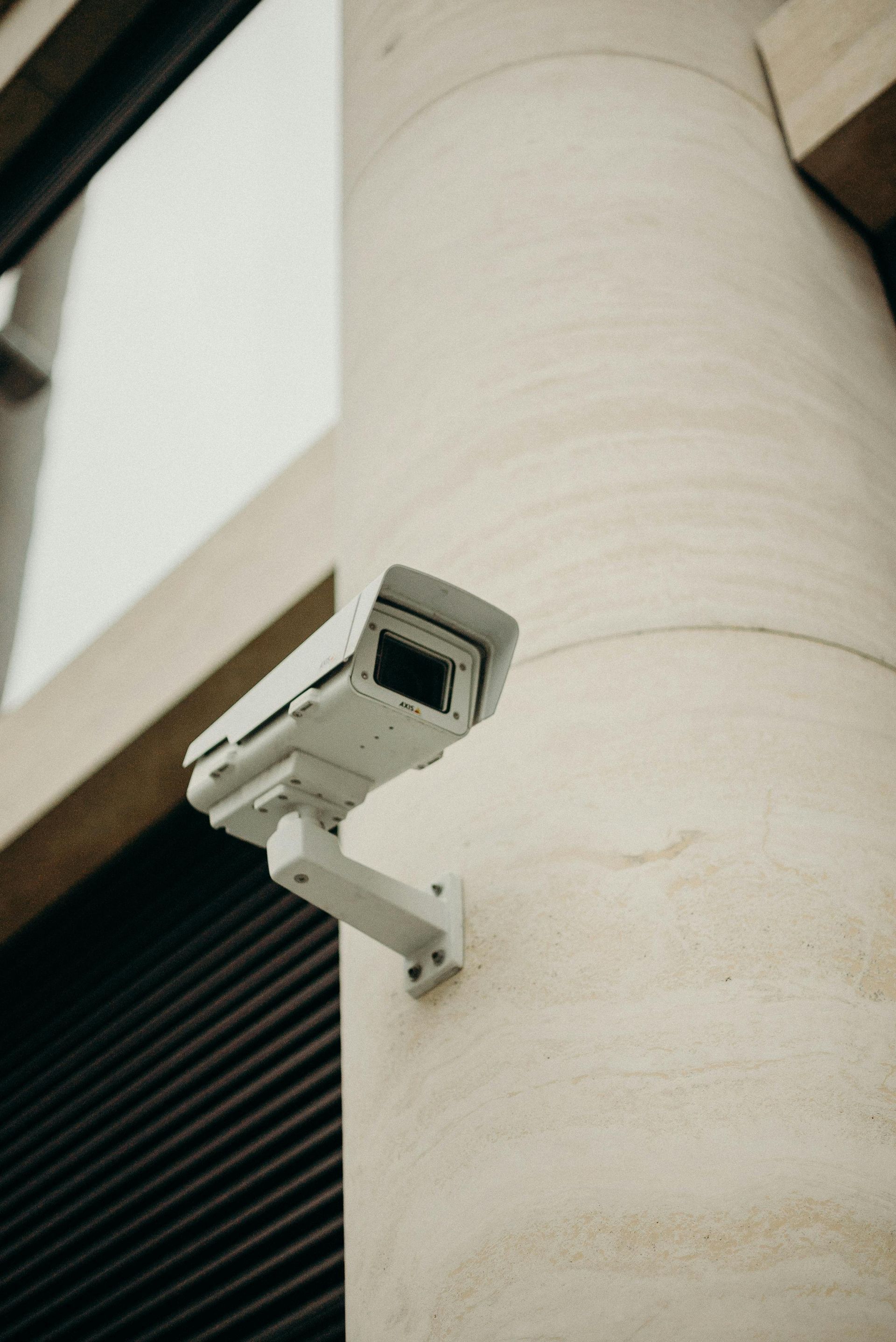 Security camera mounted on a beige, textured column, angled towards the viewer.