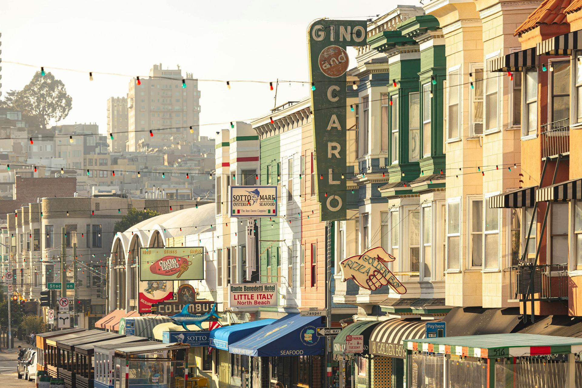 Cable cars and colorful buildings line a San Francisco street, with a Gino and Carlo sign.