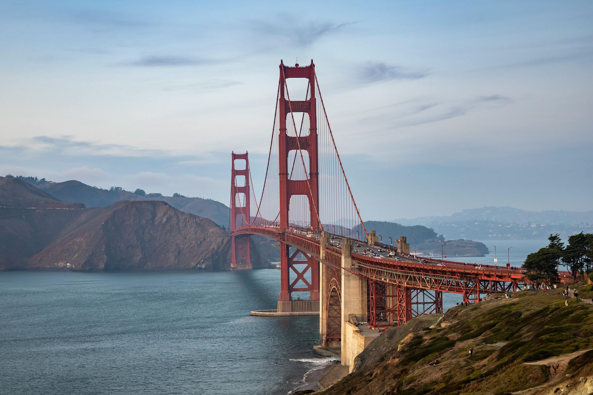 Golden Gate Bridge spanning a bay, with reddish-orange towers and suspension cables; overcast sky.