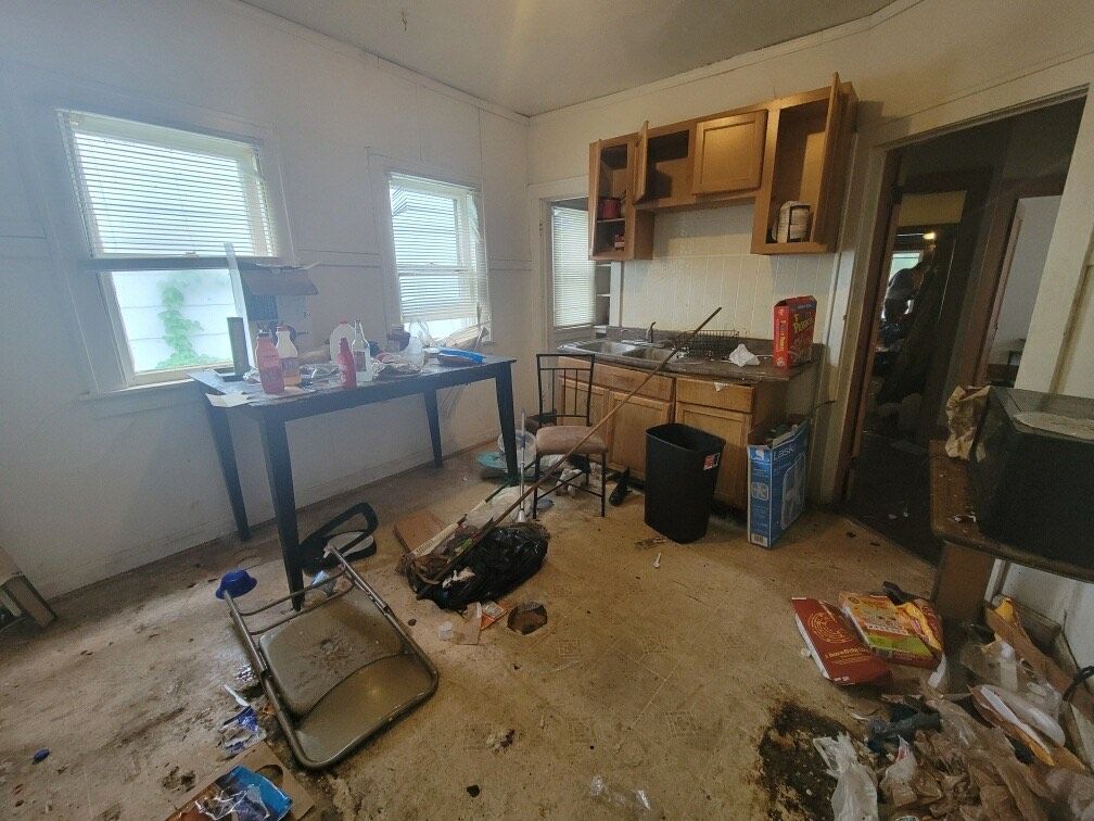 A messy room with a table , cabinets , and a sink.