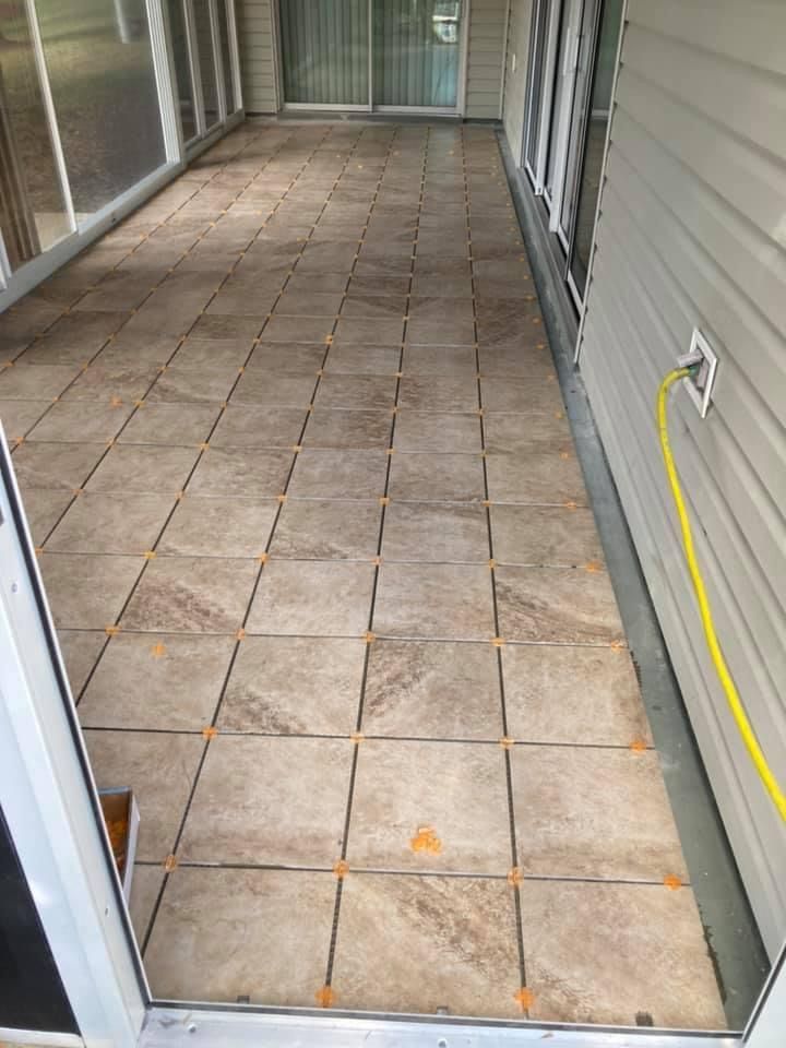 A tiled walkway leading to a house with a yellow hose attached to it.