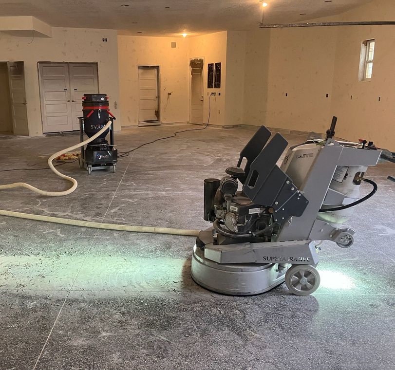 Floor grinding machine in use in a room under construction, with a vacuum hose attached.