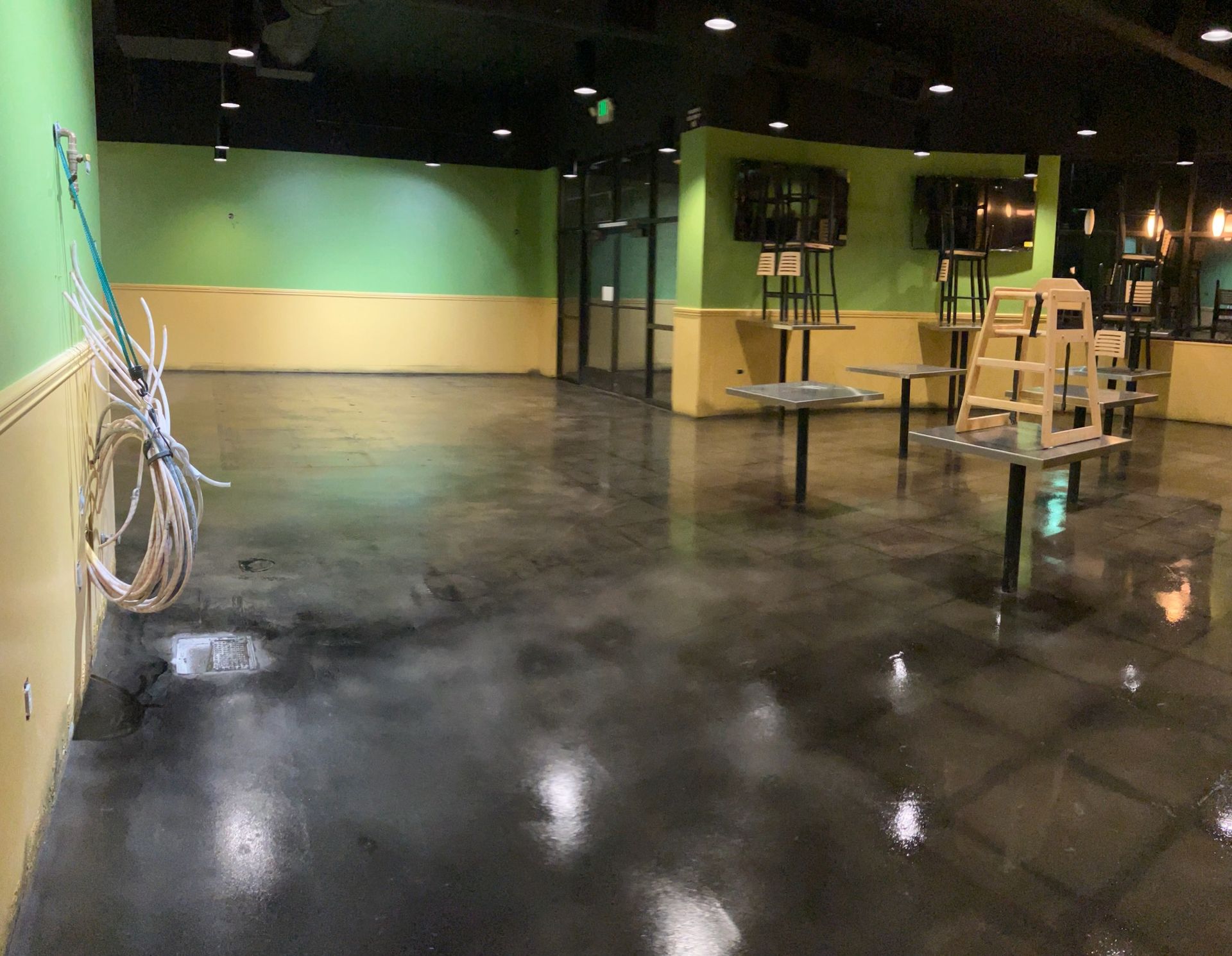 Empty restaurant interior, polished concrete floor, green and yellow walls, tables, chairs.