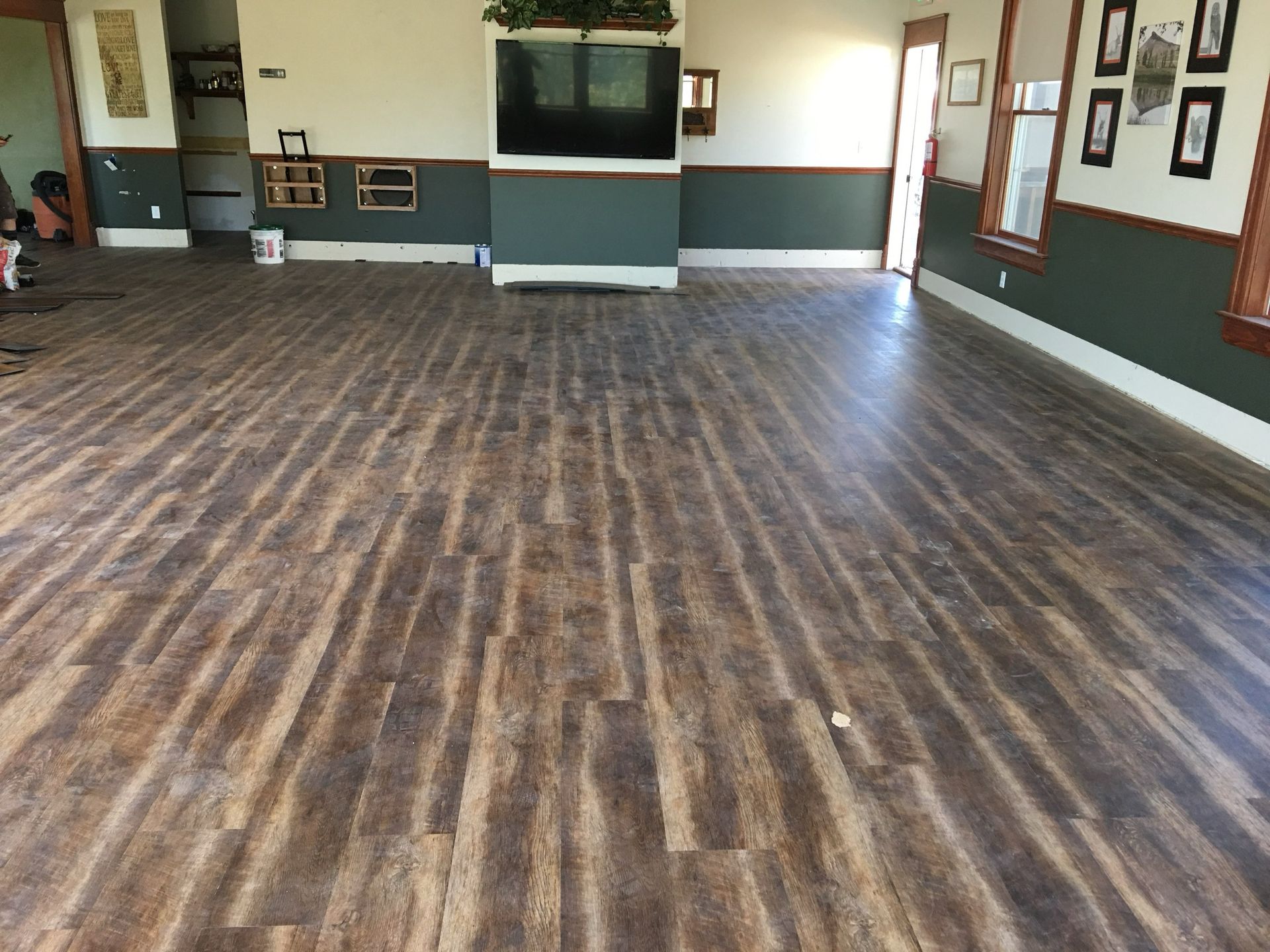 Wood-look flooring in a large room with dark green walls, a fireplace, and framed pictures.