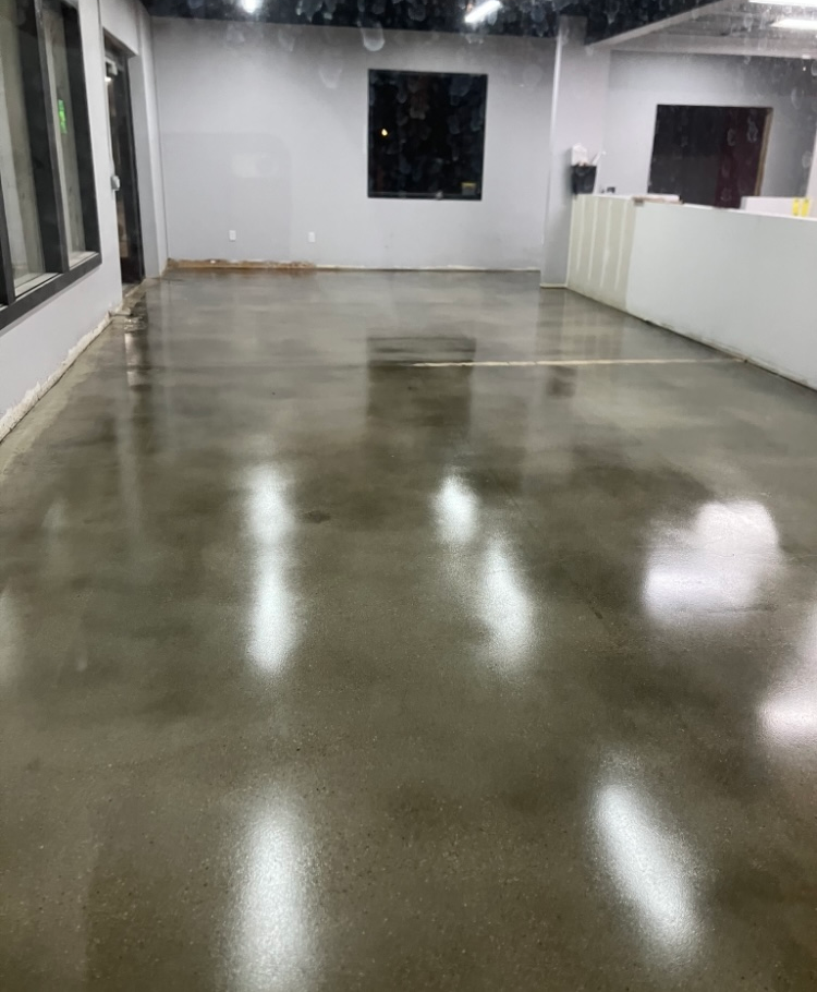 Polished concrete floor reflecting overhead lights in an empty, gray-walled room.
