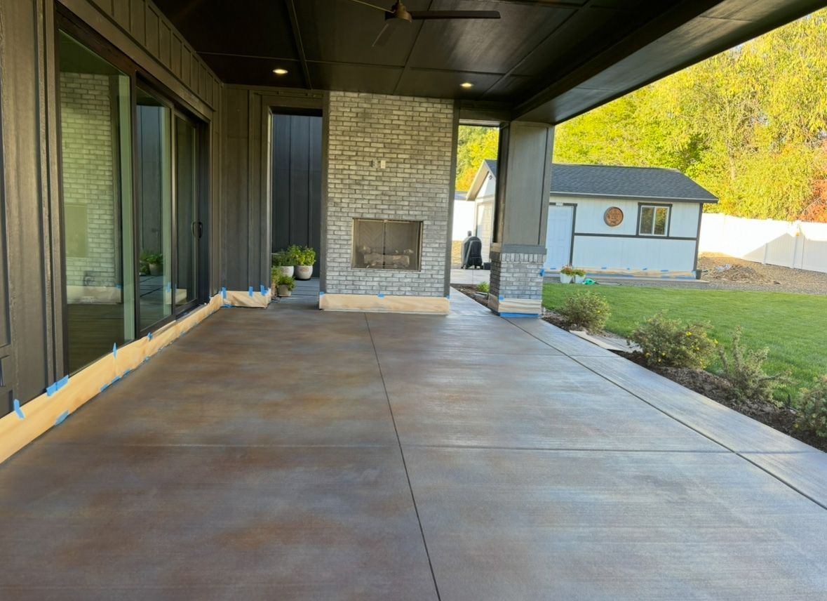 Covered patio with a fireplace, concrete floor, and a view of a yard and building.