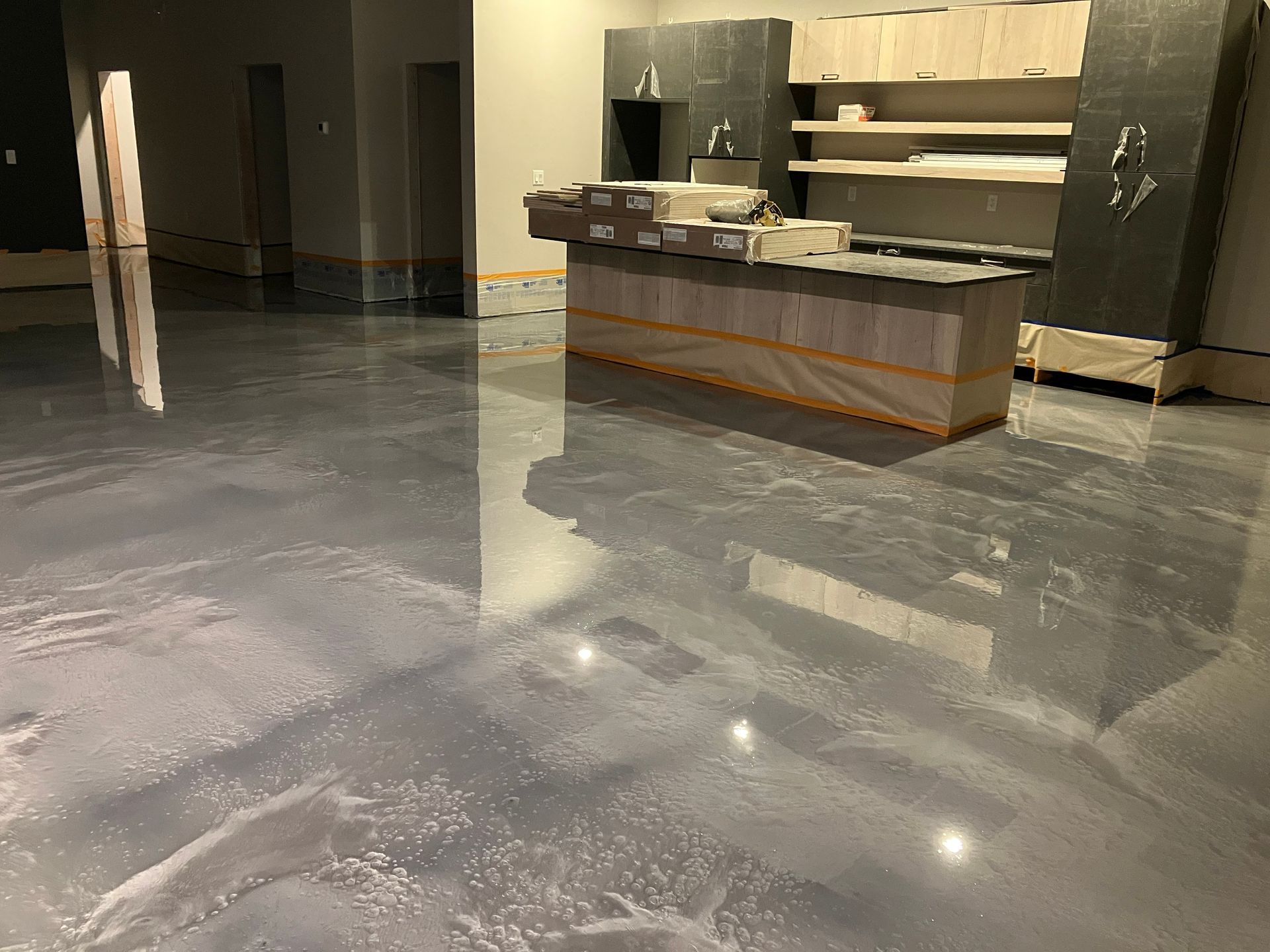 Gray epoxy floor in a room under construction, reflective, with a kitchen island and cabinets.