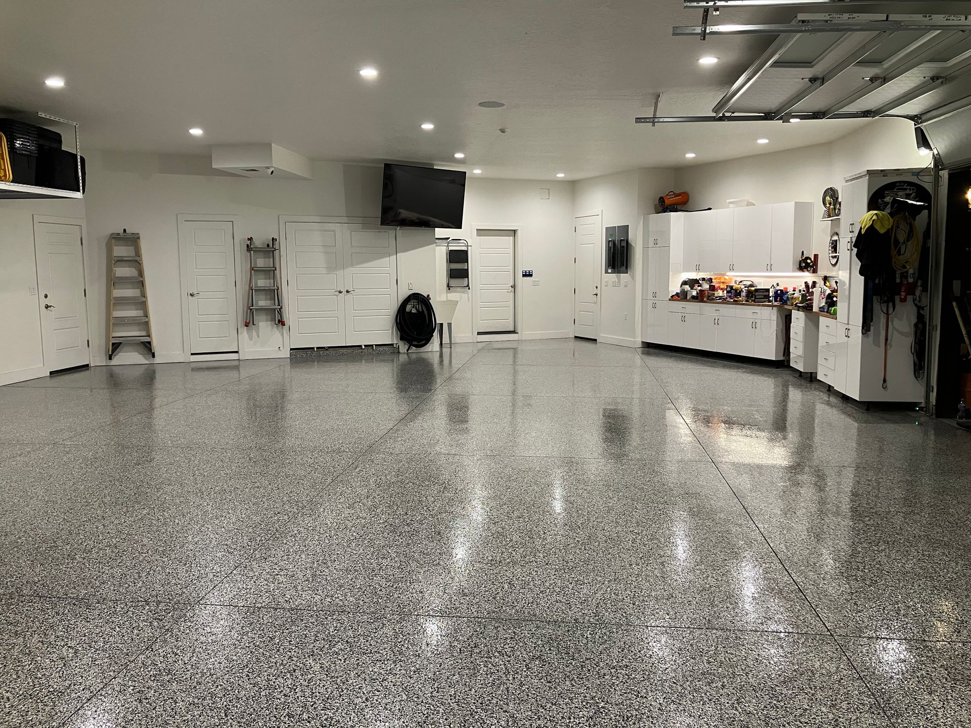 Spacious garage with epoxy flooring, white cabinets, and tools, lit by overhead lights.