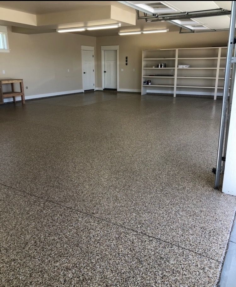 Spacious garage with speckled epoxy floor, white shelves, and two doors. Open garage door on right.