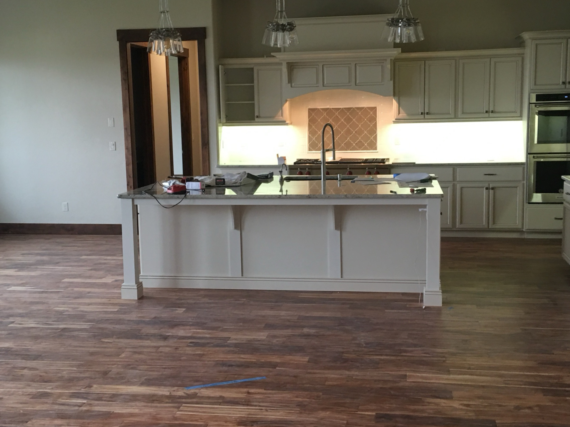 Kitchen with wood floor, white cabinets, island, and overhead lights.
