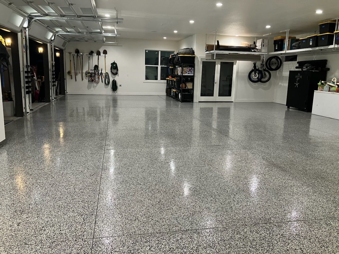 Spacious garage with speckled epoxy floor, tools, shelves, and open garage door.