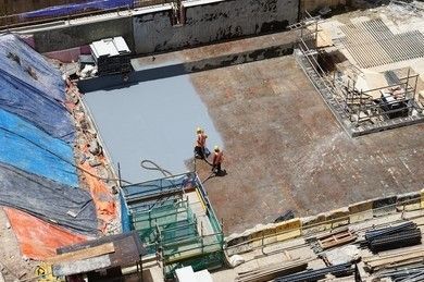 Construction workers spraying a grey coating on a concrete surface in a partially built building.
