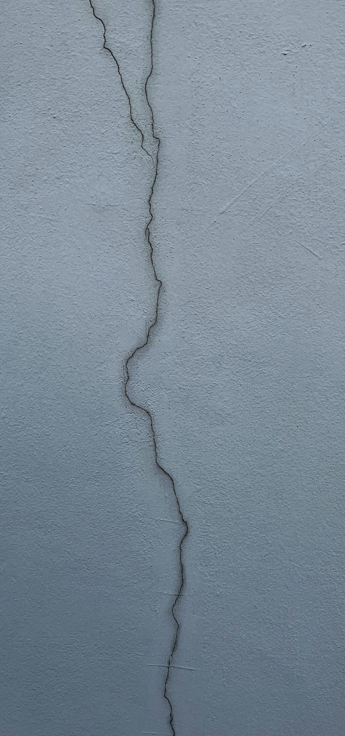 A gray textured wall with a long, vertical crack running through the center.