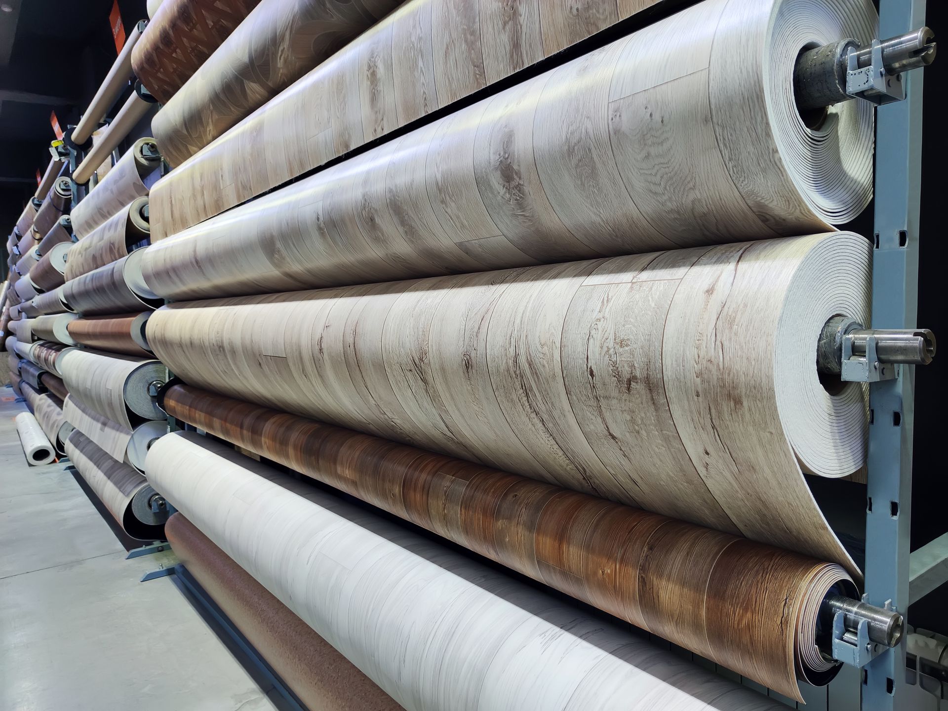 Shelves stacked with rolls of vinyl flooring in various wood grain patterns.