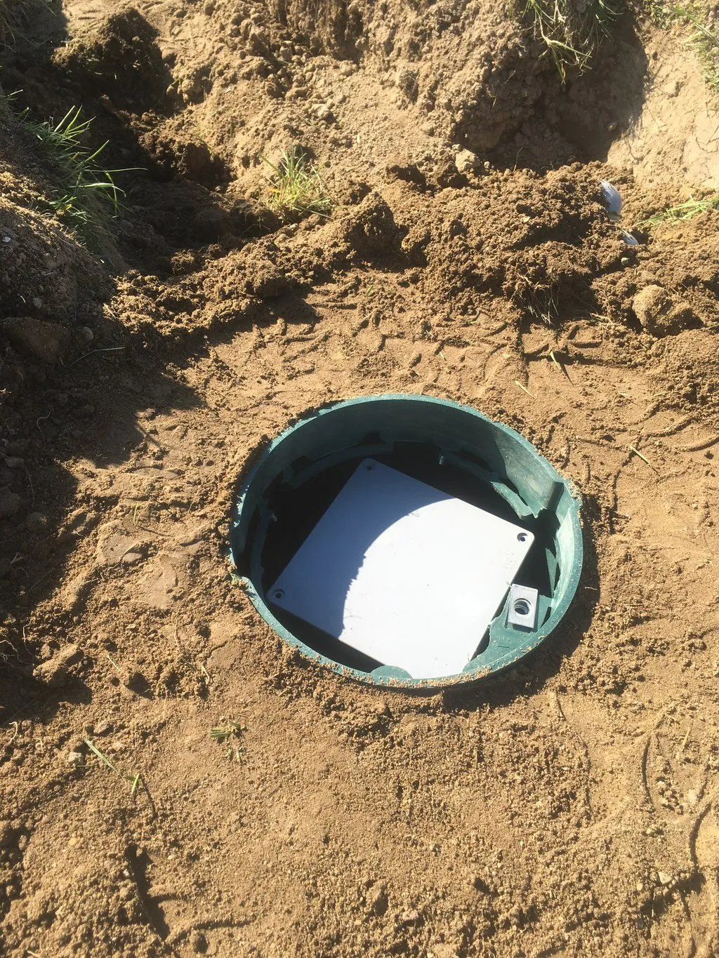 Open green access port in dirt. White lid partially visible inside.