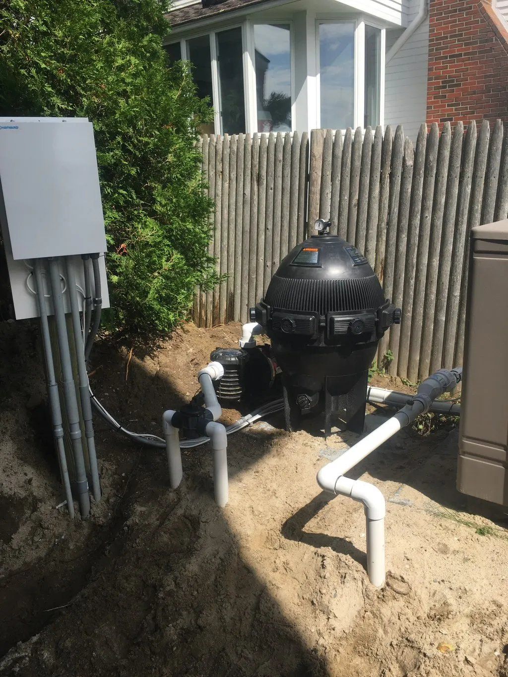 Pool filter equipment next to a wooden fence and a white house.