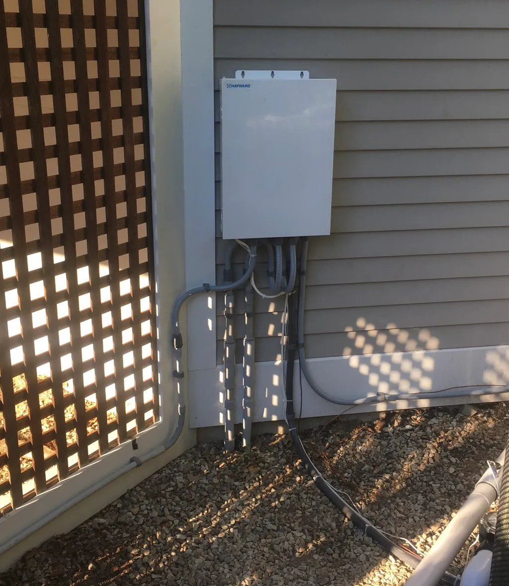 White electrical box mounted on a beige building with conduit cables running to it.