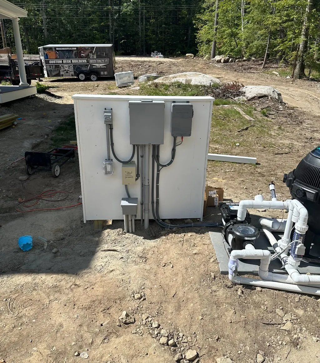 Outdoor electrical panel with conduit, connected to pool equipment on gravel.