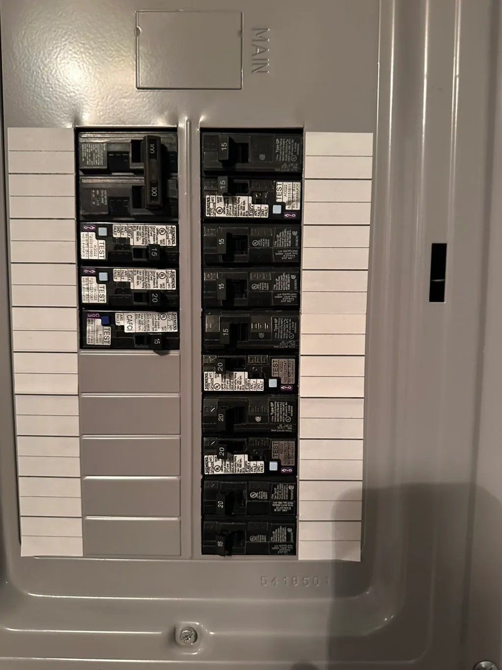 Electrical panel with numerous circuit breakers, silver in color, with white labels.