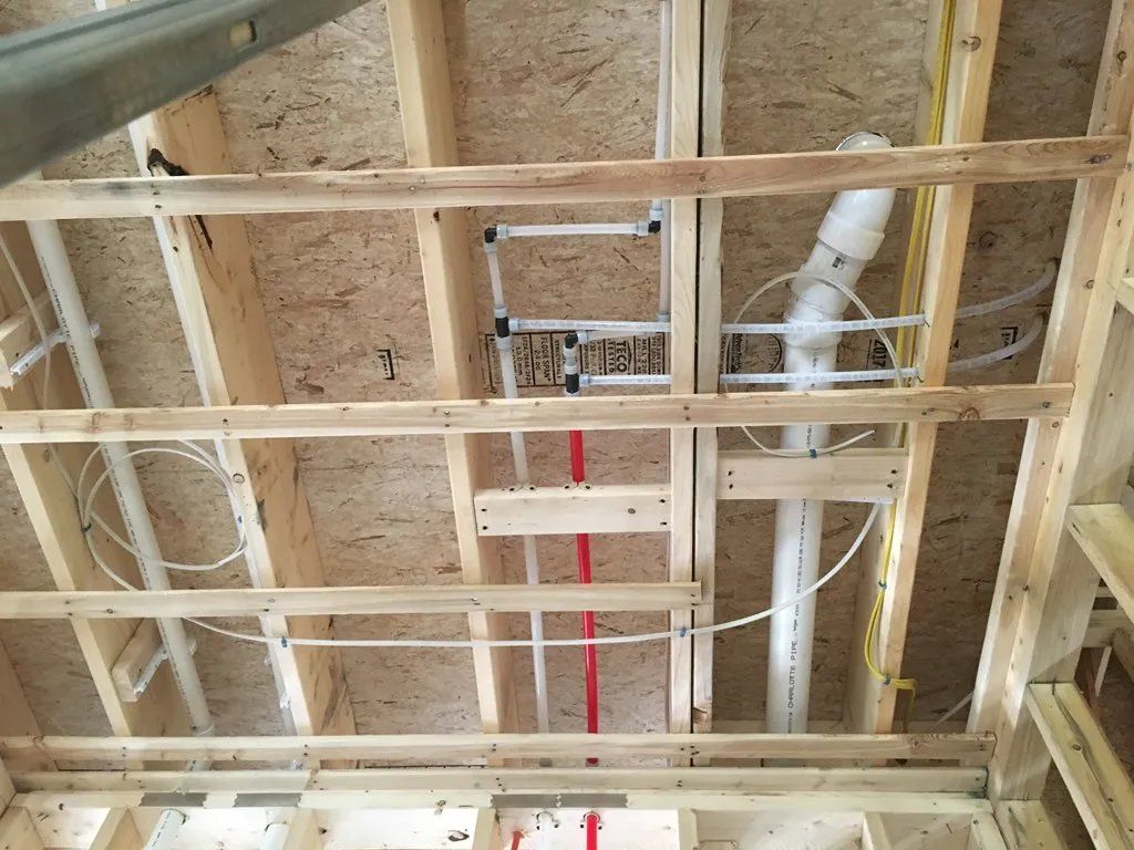 Wooden ceiling framing with plumbing pipes and wires.