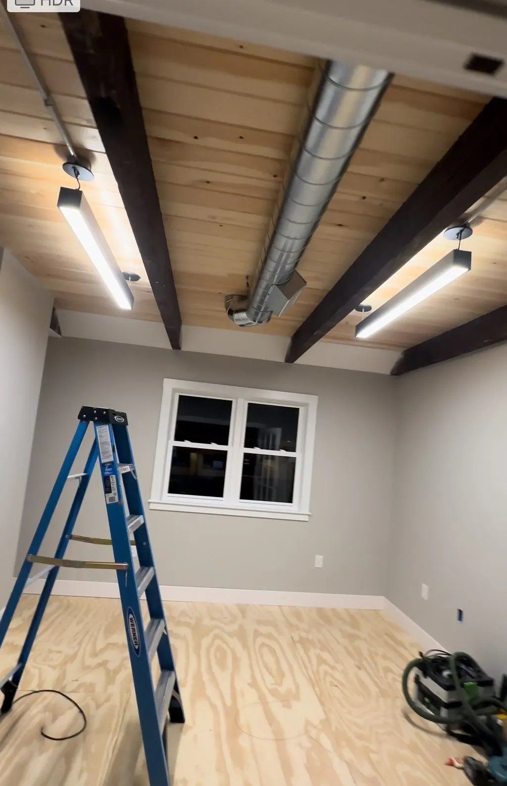 Interior room with wood ceiling, metal ductwork, and lighting. A-frame ladder, window, and saw on the floor.