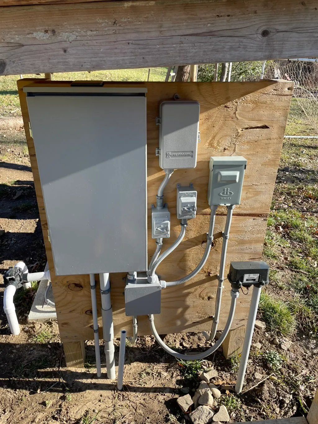 Electrical control panel mounted on plywood outdoors. Gray boxes, conduit, and wiring visible.