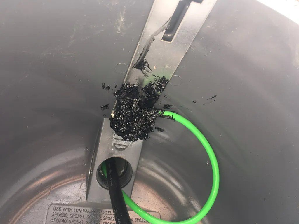 Black electrical component damage in a gray container; green and black wires extend from the damage.