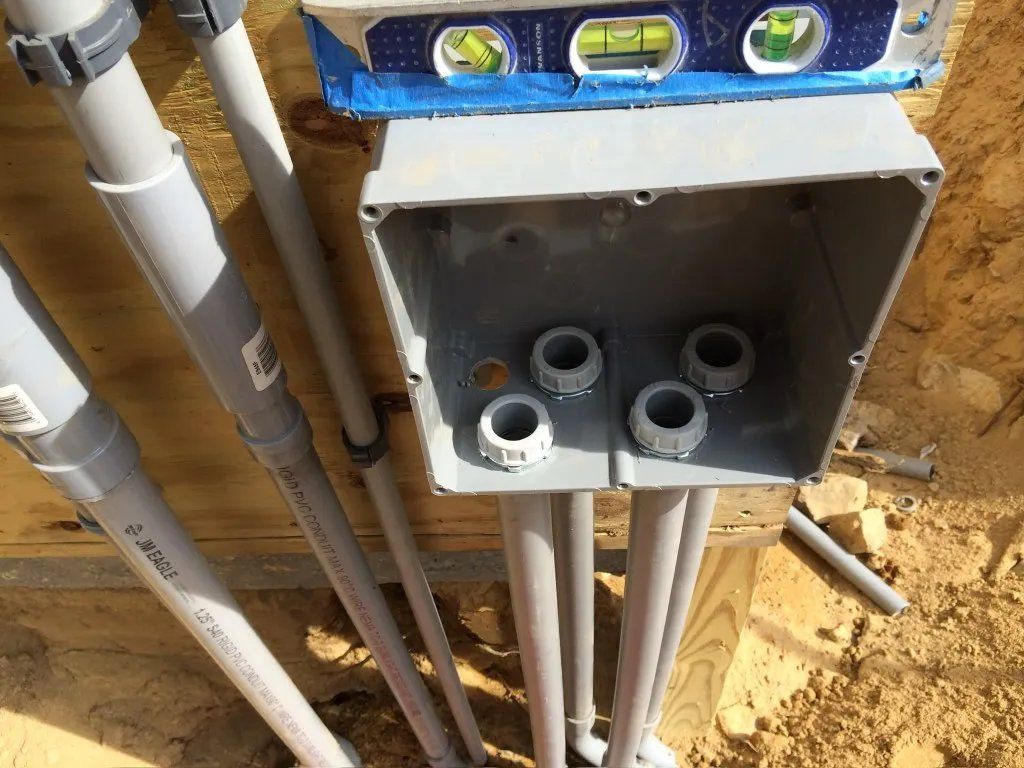 Electrical junction box with conduits and level on top, installed on wooden structure.