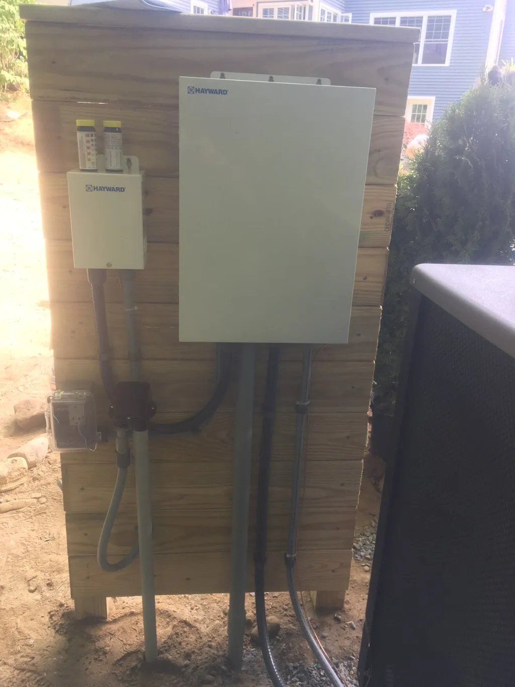 White electrical equipment mounted on wooden enclosure outdoors.