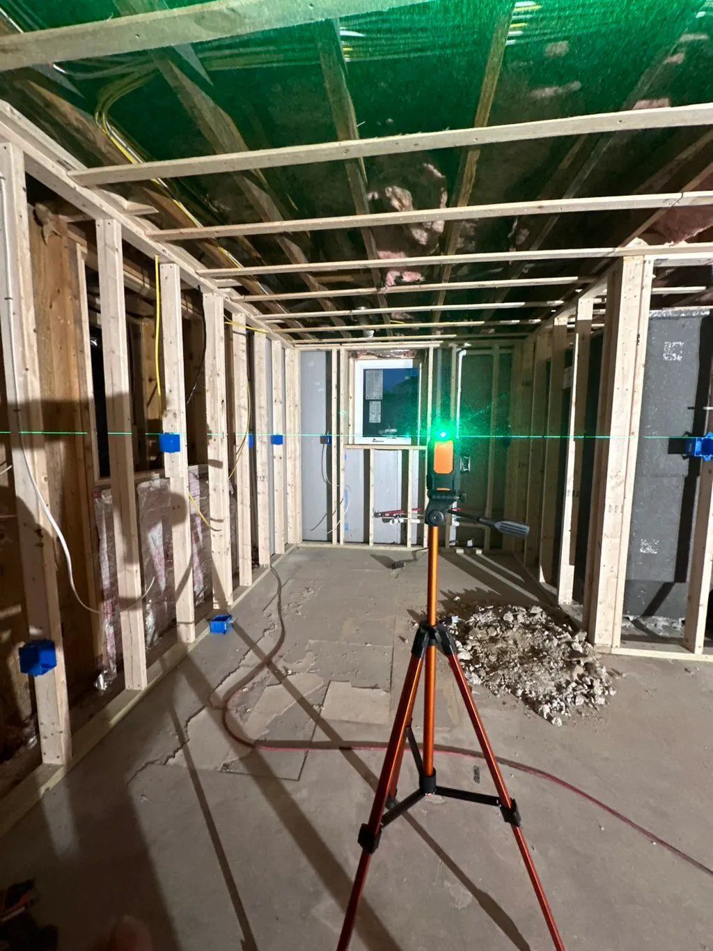 Interior framing with green laser level set on a tripod, showing level lines.