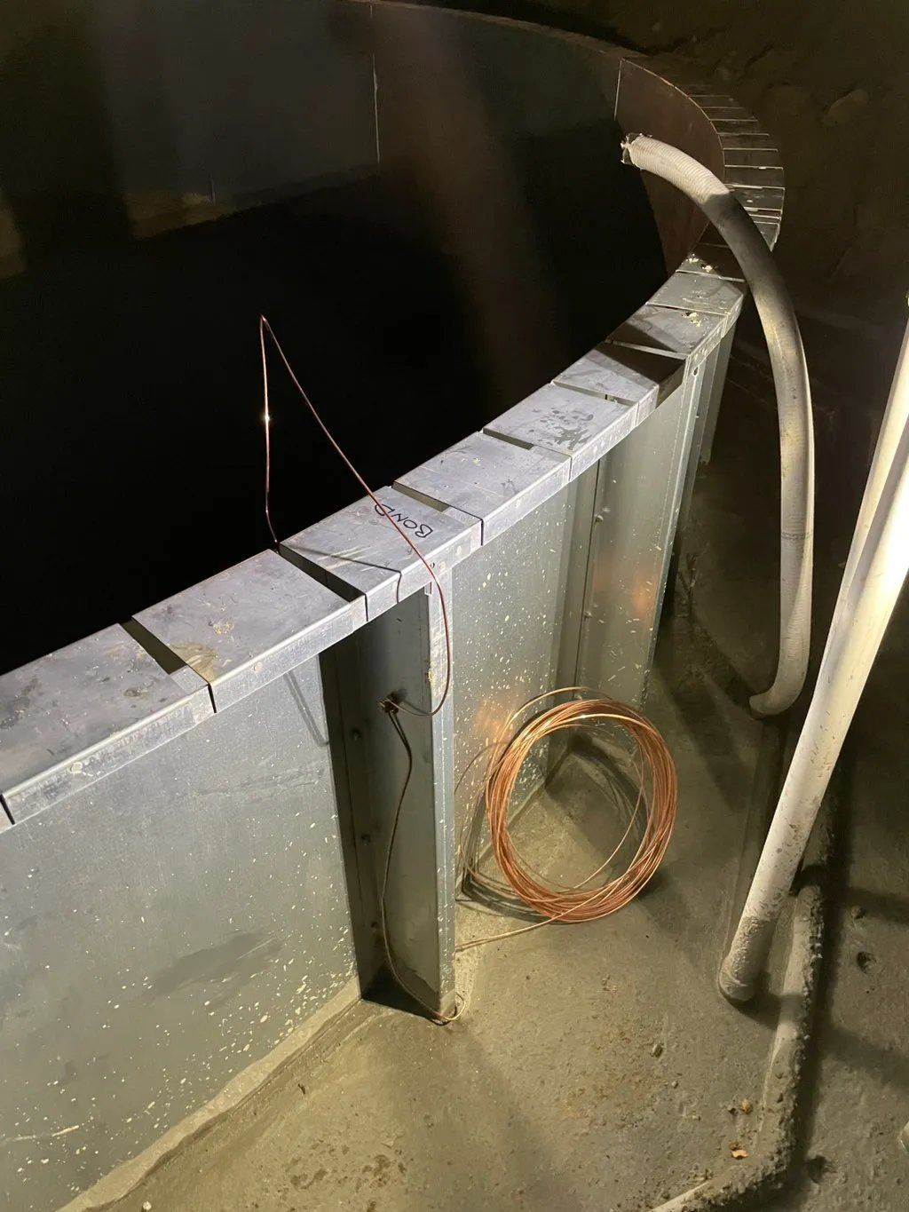 Metallic structure with copper wire coil and tubes; dark interior.